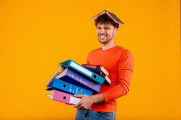 Young handsome happy man office worker with book on his head, holding document folders, isolated...
