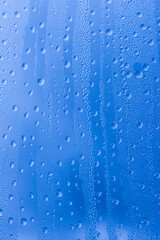 Naklejka na ściany i meble Close-up of raindrops on a window pane. Gloomy wet weather. Drops of water on glass in front of dark blue rain clouds. Rain. Abstract background texture. High quality photo