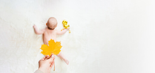 Baby cute child banner. Happy cute baby kid girl lying on white bed background. Mother hand holding yellow leaf. Light background. Little child. Serious emotion.