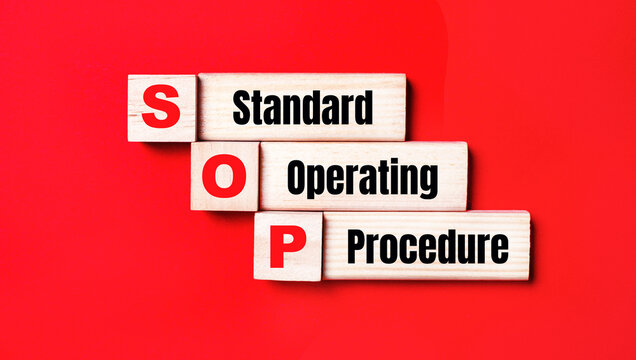 On a bright red background, wooden cubes and blocks with the text SOP Standard Operating Procedure. Manufacturing of wooden toys.