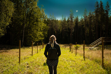 walk of a light-haired woman dressed in black with a backpack in the bosom of nature - a landscape park in Finland