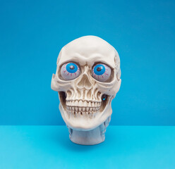Realistic human skull with bright blue eyes making silly face. Funny spooky Halloween composition.