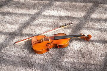 Violin, classic string instrument with bow, on light brown carpet. Orchrestra music instrument for learning on floor with window light.