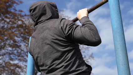 an athlete in a gray sports hoodie pulls up on a bar against a bright blue sky. crossfitter...