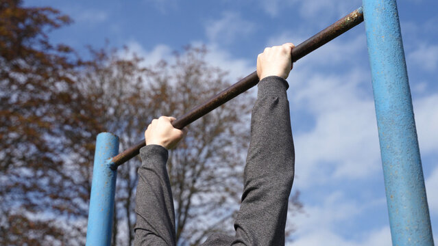 an athlete in a gray sports hoodie pulls up on a bar against a bright blue sky. crossfitter training. pumping up the muscles of the back and arms sports training on the open field calisthenics workout