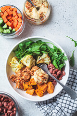 Winter vegan buddha bowl with tofu, beans, baked vegetables, hummus and beans.