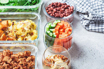 Vegan meal prep containers with  marinated tofu, beans, baked vegetables, green salad and vegetable sticks.