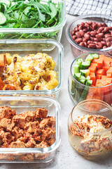 Vegan meal prep containers with  marinated tofu, beans, baked vegetables, green salad and vegetable sticks.
