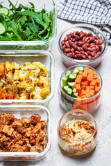 Vegan meal prep containers with  marinated tofu, beans, baked vegetables, green salad and vegetable sticks.