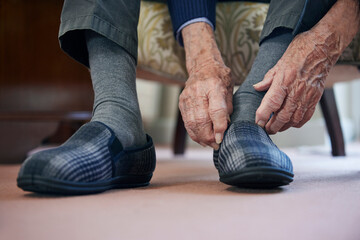Close Up Of Senior Man Putting On Slippers To Keep Feet Warm In Cost Of Living Crisis - obrazy, fototapety, plakaty