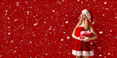 Woman wearing stylish red dress of Christmas costume posing with gift box in snow