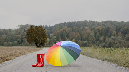 Rote Regenstiefel und bunter Regenschirm auf einem Weg