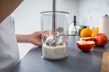 Woman using hand blender to mix fresh fruit smoothie in kitchen