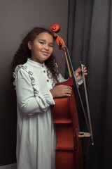 Beautiful girl in a stylish dress stands with a cello.