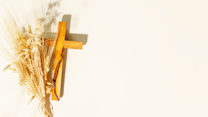 Wooden crucifixion with bouquet of wheat and rye on light background with copy space. Religion...