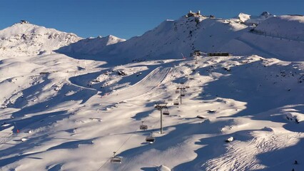 Zermatt, Switzerland: Aerial footage of the famous Zermatt ski resort with a chairlift and skiers and snowboarders on the slope of the Gornergrat ridge in the Swiss alps on a sunny winter day. 