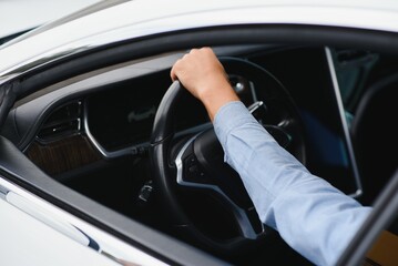 Businessman holding steering wheel while driving modern electric car on the street road. Confident man driving expensive car. Driver Turning Steering Wheel In Luxurious Auto On Trip