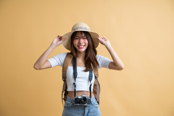 Obraz na płótnie Canvas young attractive Asian woman traveler in casual clothes wearing straw hat with backpack and camera isolated on yellow background, Tourist girl having cheerful holiday trip concept
