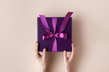 Female hands with festive minimalistic manicure holding out a violet gift box. Christmas Eve Surprise. Xmas and New Year love sharing. Black Friday sales, Birthday celebration party concept