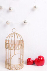 Valentines Day   greeting card. Decorative golden  cage with burning candle and decorative hearts against white textured wall. 