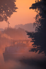 Silhouette of a cargo boat in the fiery red fog on a misty Morning on the River during sunrise....