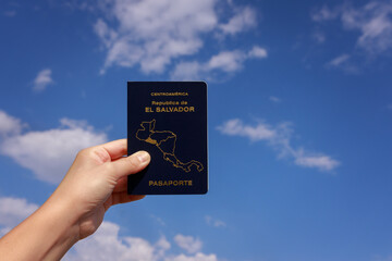 The hand of an invisible person holds the passport of El Salvador against the sky with clouds. High quality photo