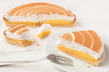 Cut up lemon tart with meringue topping next to a portion of lemon tart on plate with a fork.
