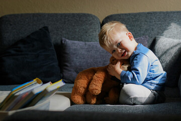 Obraz premium little boy playing on sofa and hugging stuffed teddy bear 