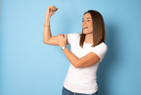 Side view of funny young brunette woman girl in white t-shirt posing isolated on blue background studio portrait. People lifestyle concept. Mock up copy space. Showing biceps, muscles