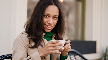 Fototapeta premium Young smiling african american girl drinking coffee in a cozy cafe. Holidays, lunch time and vacation concept 