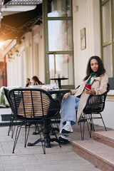 Young smiling african american girl using smartphone in a cozy cafe. Holidays, lunch time and vacation concept  