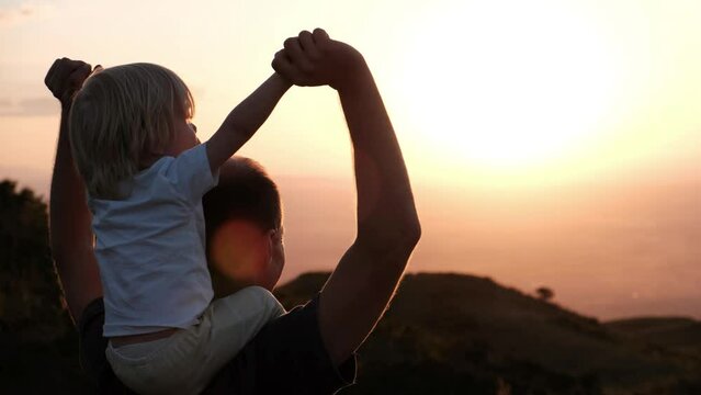 father with a cute son on his shoulders at sunset look at the camera