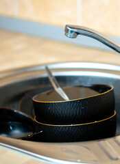 A pile of dirty dishes in the sink. Black dishes are stacked in a metal sink in the kitchen. Washing dishes, house cleaning.