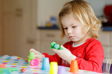 Adorable cute little toddler girl with colorful clay. Healthy baby playing and creating toys from play dough. Small kid molding modeling clay and learning