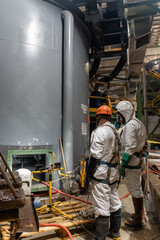 Workers in special chemical overalls near an open container of cyanide. The tank is being cleaned.