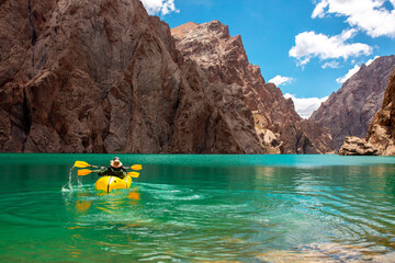 Kayaking on a mountain lake. Two men are sailing on a red canoe along the lake along the rocks. The...