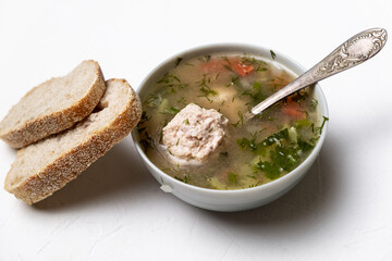 Vegetable soup with meatballs in a plate on a white background. Two slices of bread side by side.