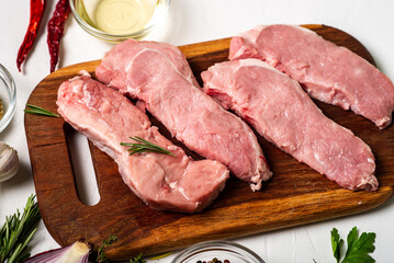 Raw meat steaks on a cutting board. White background. Preparation for cooking pork meat. Various spices, seasonings lie nearby.
