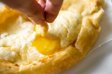Adjarian Khachapuri. A hand dips a piece of dough into an egg yolk. Traditional Georgian dish with cheese and chicken egg.