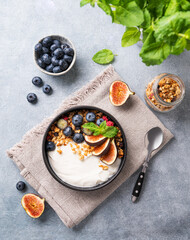 Fototapeta na wymiar Natural yogurt with muesli, berries and figs in a black bowl on a blue background with mint. Healthy and nutritious breakfast