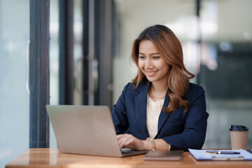 Portrait of smiling Asian businesswoman enjoying her work on her laptop at the office.