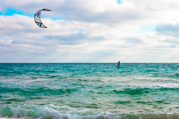 A man rolls on the waves on a board with a parachute, kitesurf on the sea on an autumn cloudy day. Sports and Hobbies