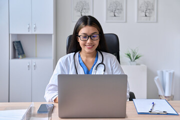 Young Asian female doctor looking at laptop screen holding online consultation