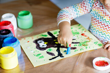 Closeup of little creative toddler girl painting with finger colors an owl bird. Child having fun with drawing at home, in kindergaten or preschool. Games, education and distance learning for kids.