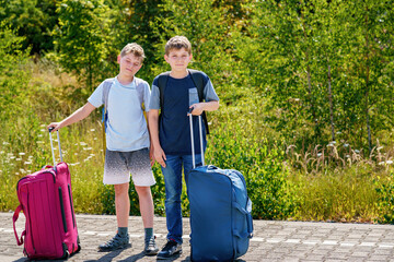 Two children, school boys with suitcases before leaving for summer vacation camp. Happy kids,...