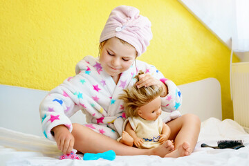 Cute smiling little girl child playing with her doll at home. Preschool child in bathrobe after...