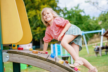 Little girl climbing on playground on summer day. Happy brave preschool child enjoying sports and...