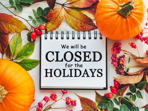We will be closed for the Holidays. Beautiful Thanksgiving sign. Bright pumpkins, tree leaves, red berries and colorful flowers lying on an empty table. Close-up, top view. Holiday concept