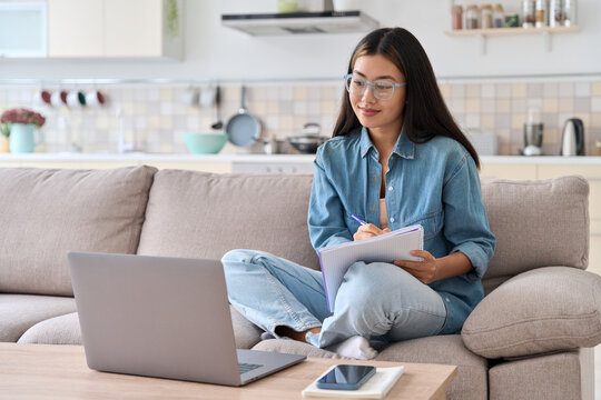 Teenager asian woman watching webinar on laptop making notes