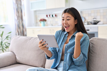 Excited asian woman celebrating success looking at digital tablet screen
